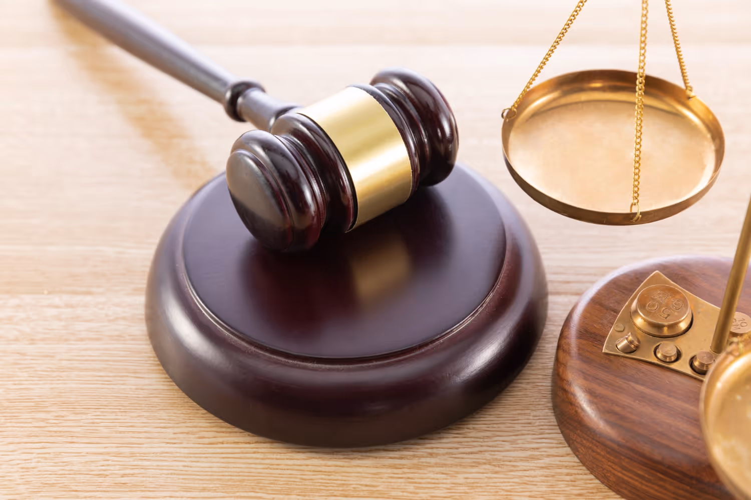 Wooden judge's gavel resting on sound block next to golden balance scales on a wooden surface.