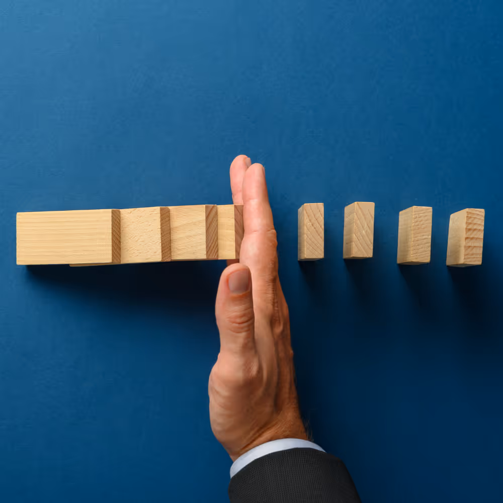 Hand stopping a row of falling wooden blocks against a blue background.