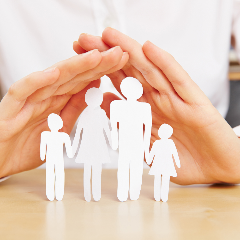 Hands forming a protective shelter over paper cutouts of a family of four holding hands.
