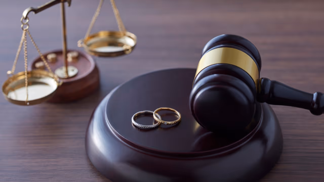 Judge's gavel resting on a wooden base with two wedding rings and a blurred scale of justice in the background.