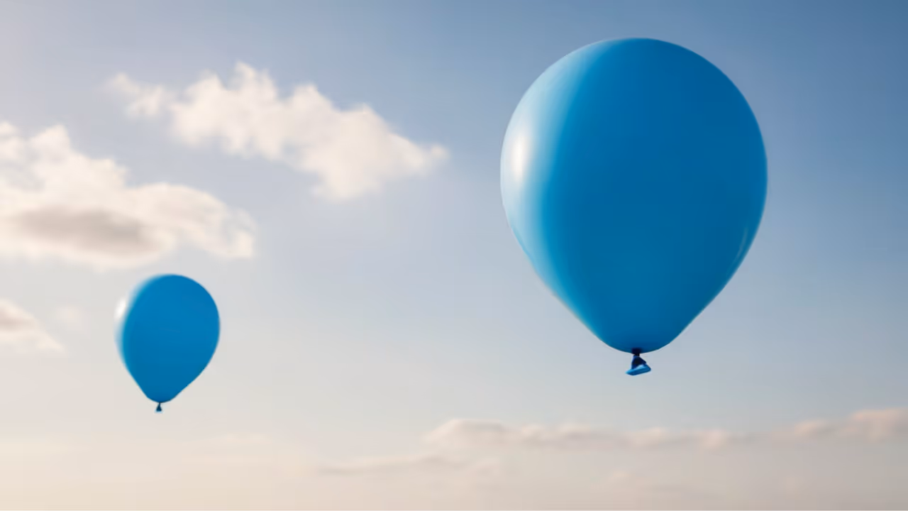 Two large blue helium balloons floating in a cloudy sky.
