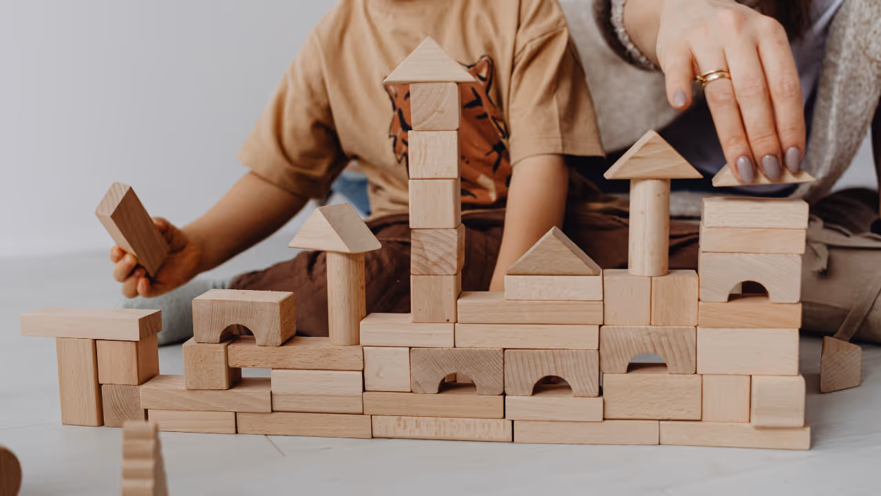 Child and adult building a structure with natural wooden blocks on the floor.