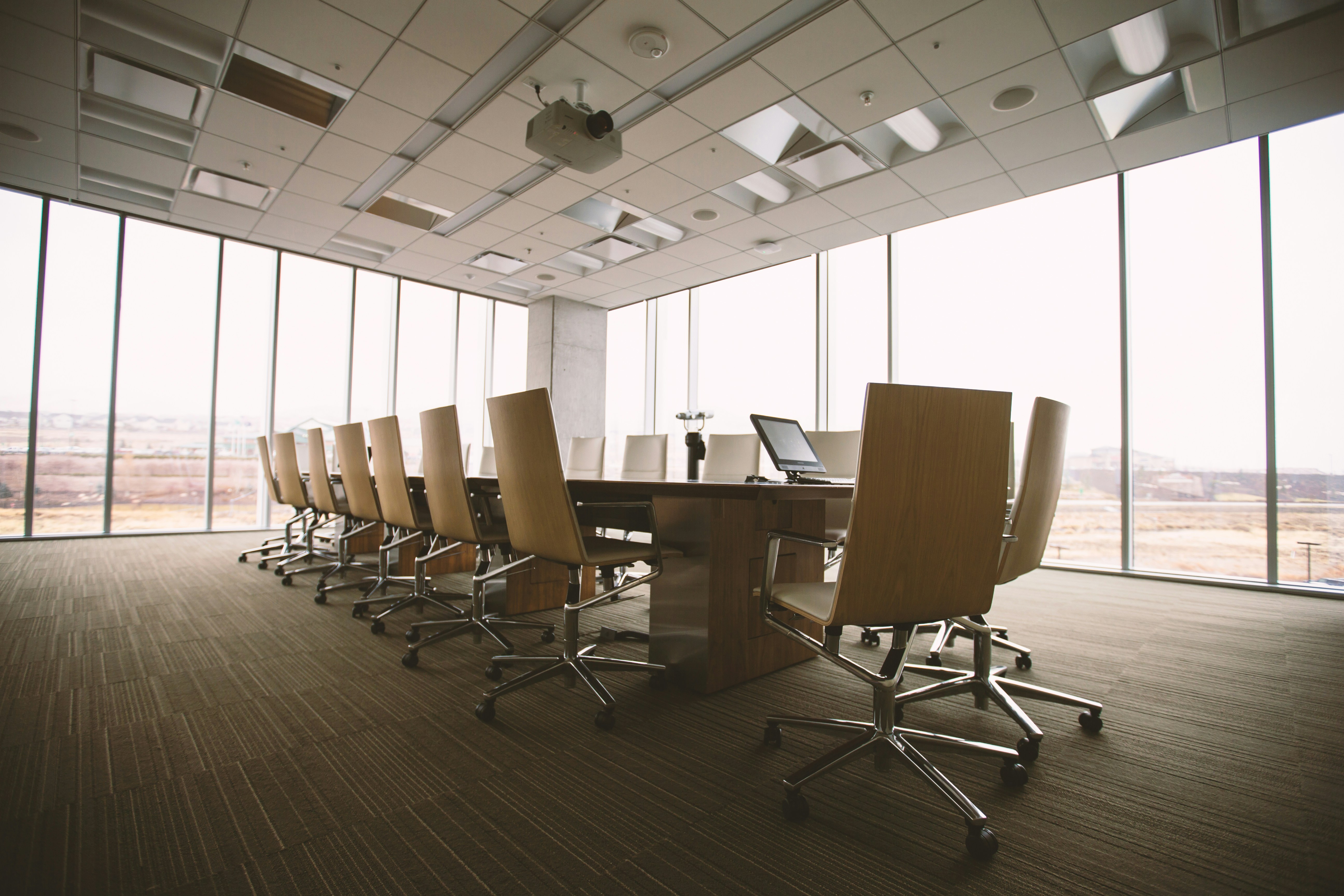 Empty modern conference room with wooden chairs around a rectangular table and large floor-to-ceiling windows.